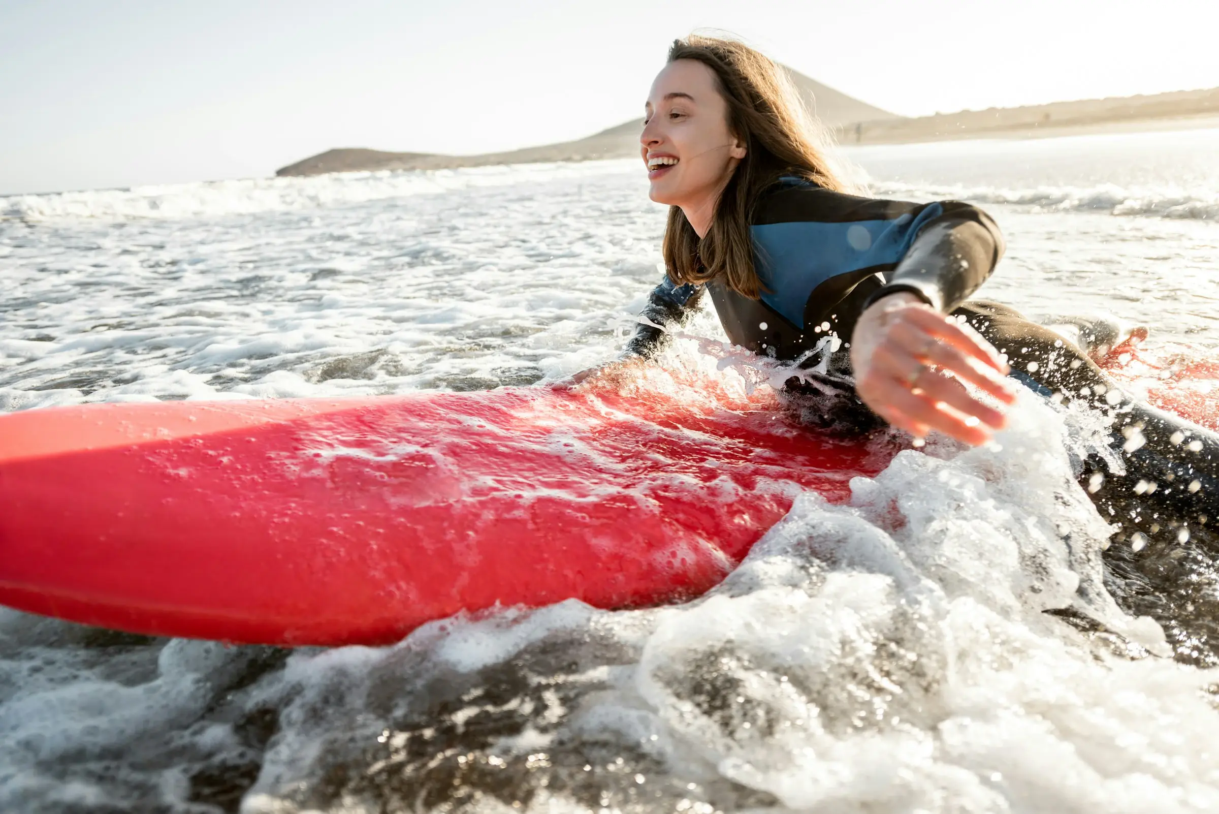 Uma surfista a rir, deitada na prancha vermelha, no meio da espuma